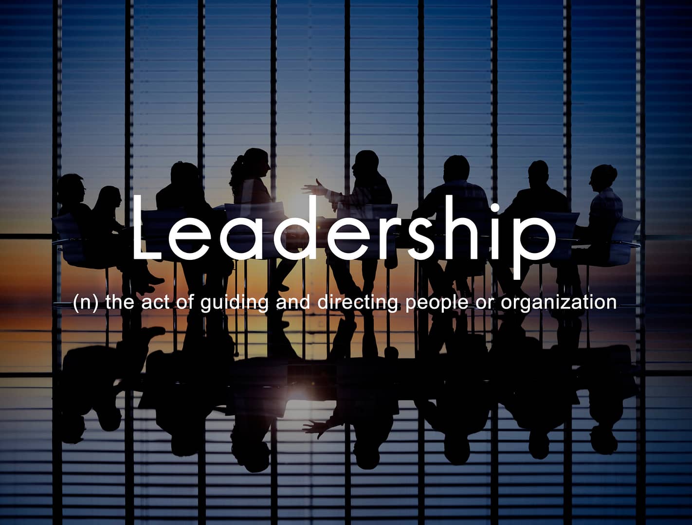A silhouetted group of professionals having a meeting in a modern conference room with large windows during sunset.